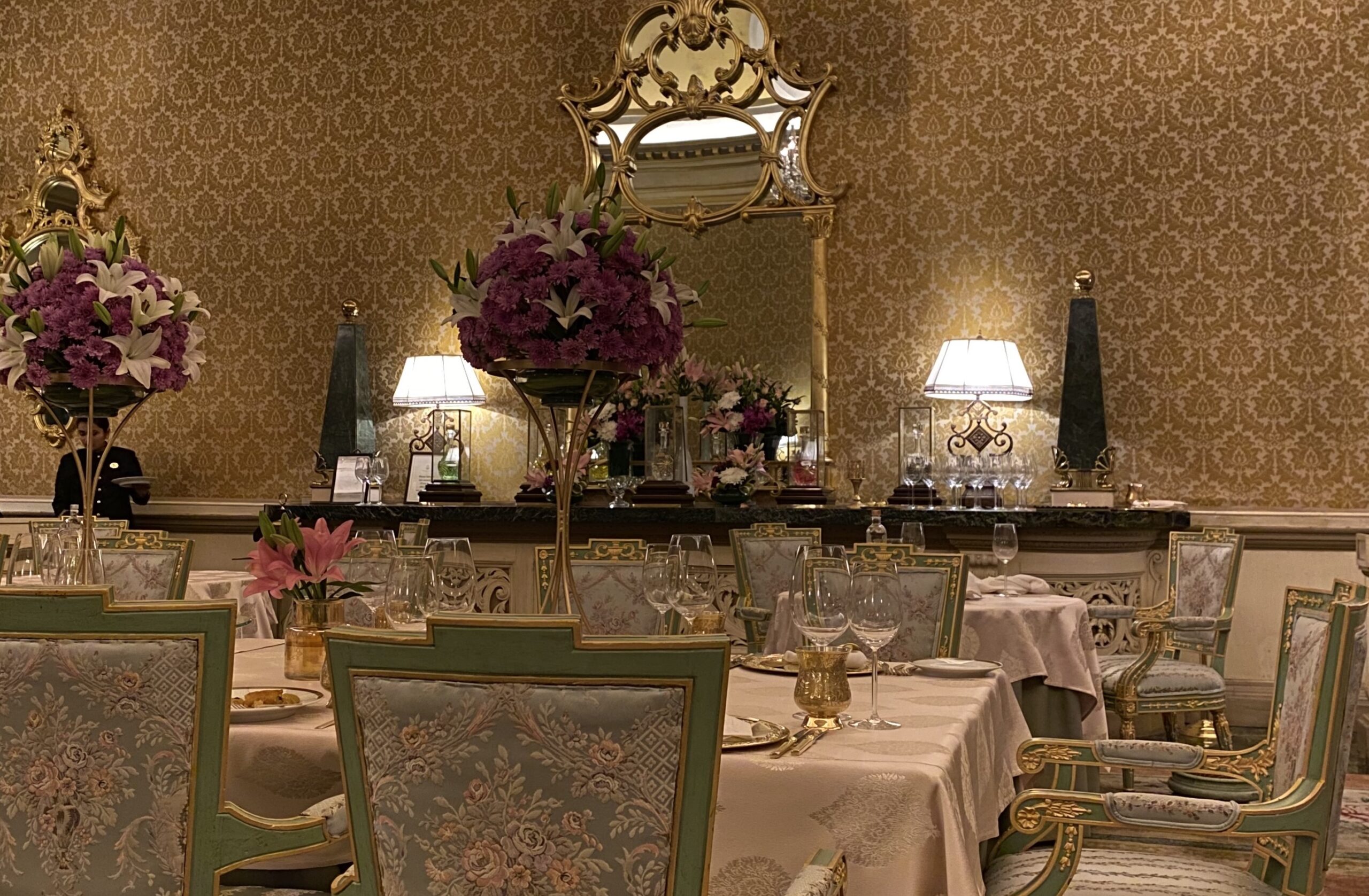 Image shows opulent gilded room with table set with gold plated tableware and flowers